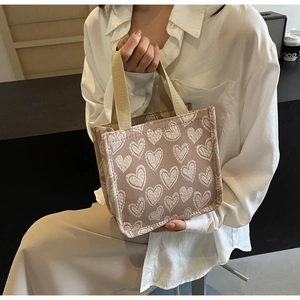 Dettaglio borsa tote in tela rosa con motivo a cuori e manici kaki su una modella