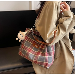 Detail of vintage plaid tote bag with brown leather straps and plush monster charm