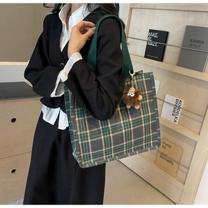 Large green plaid canvas tote bag with monster charm shown on model's shoulder