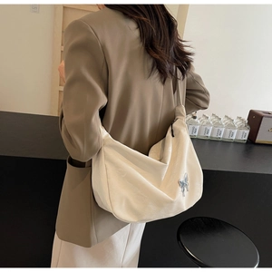 Détail d'un grand sac hobo crème avec pendentif papillon argenté porté par un mannequin
