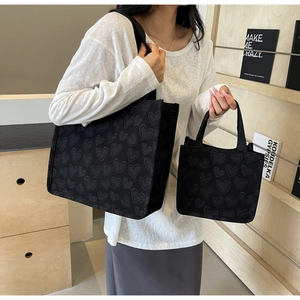 Detail of black canvas tote with heart pattern shown on a white-dressed model