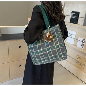 Large capacity green plaid canvas tote bag with brown plush pendant shown on shoulder