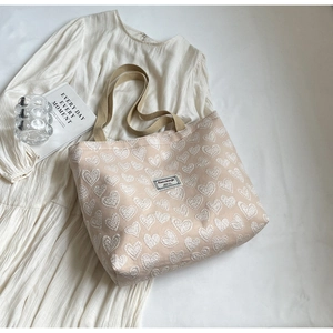 Detail of canvas tote bag featuring heart embroidery and woven straps on fabric background