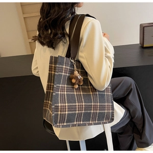 Detailed view of vintage plaid canvas tote bag with brown plush monster charm on model