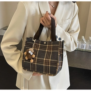 Detail of checkered canvas tote bag with brown handles and a plush monster charm