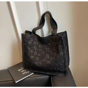 Detailed view of black tote bag with 3D floral texture on a leather sofa surface