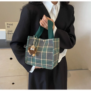 Close-up of green plaid canvas tote bag with brown plush monster charm and snap button