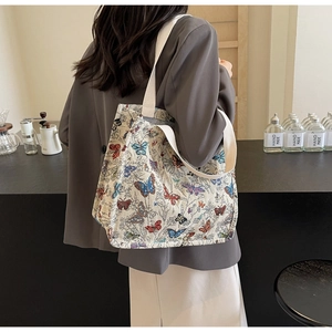 Canvas tote bag with colorful butterfly print worn by a model in a cozy cafe setting