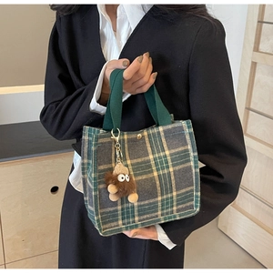 Detail of green plaid canvas tote bag with metal buckle and plush cartoon charm