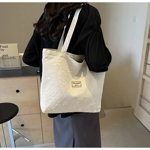 Detailed shoulder view of white tote bag featuring 3D floral texture and brand label