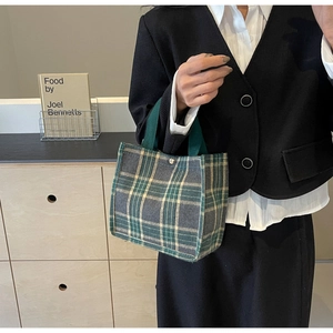 Detail of green plaid tartan canvas tote bag showing top handle and snap metal button