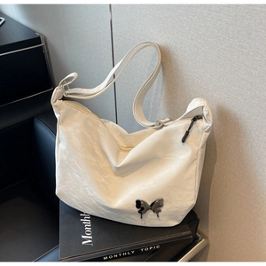 Gros plan d'un sac à bandoulière en nylon blanc plissé orné d'un papillon en métal argenté