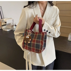 Detail view of red plaid canvas tote bag with brown plush monster charm and red straps