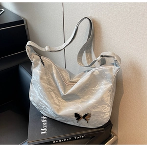Détail de la texture plissée argentée et du logo papillon en métal sur le sac