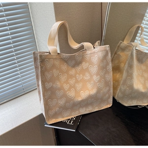 Dettaglio borsa tote beige con motivo jacquard a cuori bianchi e robusti manici in tessuto