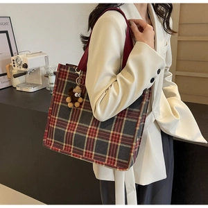 Detailed close-up of a large plaid tote bag with plush bear charm and woven strap