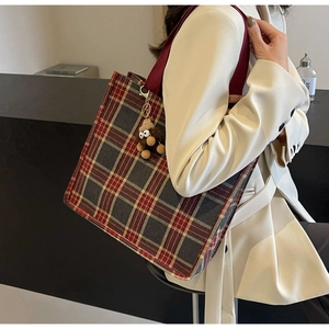 Detail of red plaid canvas tote bag with brown plush monster keychain on shoulder