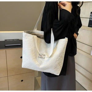 Detail of white tote bag featuring 3D floral texture and elegant brand patch design
