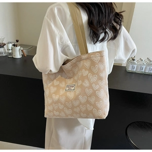 Detail of beige canvas tote bag with heart jacquard pattern and brand label on strap