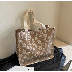 Detail of khaki tote bag featuring white floral embroidery and beige woven handles