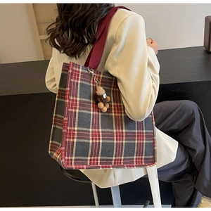 Detail of red and grey checkered canvas tote bag with burgundy strap and bear charm