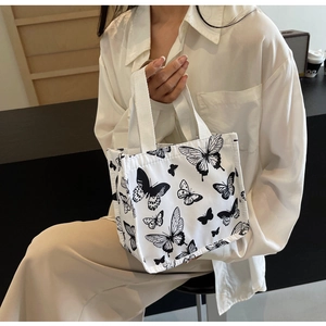 Close-up of white canvas tote bag with black butterfly patterns worn over the shoulder