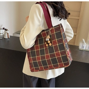 Detail of red plaid tote bag with wide strap and plush monster charm on model