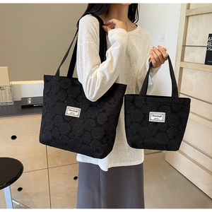 Detailed view of black tote bag with embossed rose jacquard texture and square label