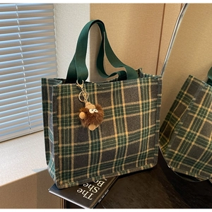 Detailed view of green plaid tote bag with wide handles and a plush monster charm