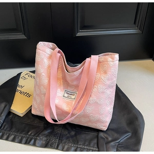 Detail of pink canvas tote bag featuring white heart patterns and woven shoulder straps