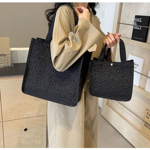 Detail of black floral textured tote bag set with wide shoulder strap and metal buckle