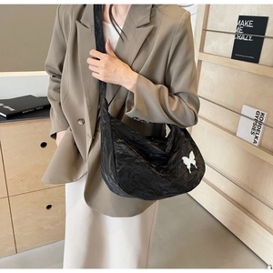 Détail d'un sac bandoulière plissé noir avec écusson papillon dans une scène de vie