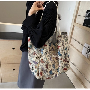 Detail of a beige canvas tote bag with colorful butterfly embroidery and logo tag