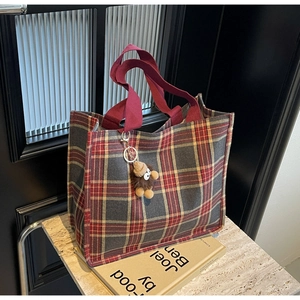 Detail view of retro plaid tote bag with red handles and brown plush monster charm