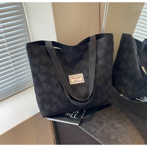 Close-up of black tote bag with heart-shaped jacquard pattern and woven brand patch