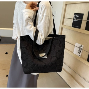Detail of black tote bag showing 3D rose floral jacquard texture and woven strap