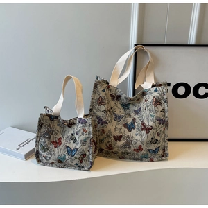 Detail view of large and small butterfly jacquard tote bags on a minimalist display