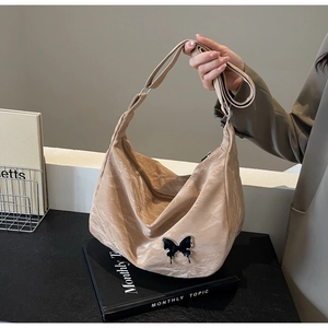 Détail du sac à bandoulière abricot avec texture plissée et décor papillon en métal