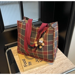 Detail of red checkered canvas tote bag with plush doll charm on marble tabletop