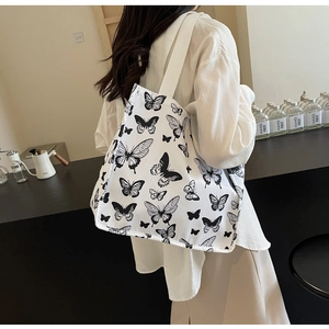 Detailed view of white canvas tote bag with black butterfly prints worn by a model