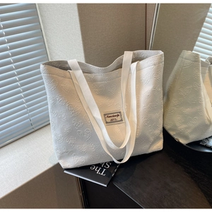 Close-up of white canvas tote bag featuring textured heart jacquard and fabric label