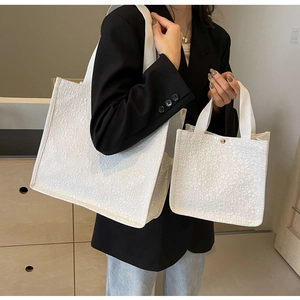 Detail of white textured canvas tote bags in two sizes with gold clasp and knit fabric