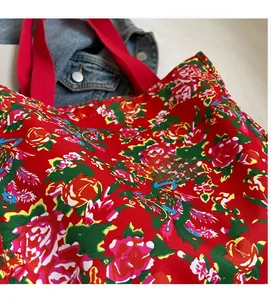 Detail of red floral tote bag with phoenix pattern and reinforced handles on denim