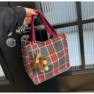 Close-up of vintage plaid canvas tote bag with red handle and plush monster charm