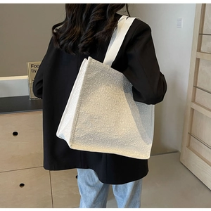 Detail showing the embossed texture and wide shoulder strap of this white canvas tote bag