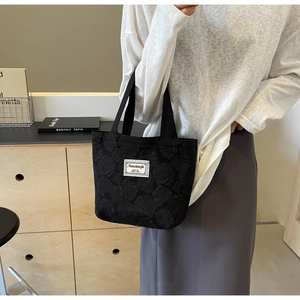 Detail of black tote bag featuring 3D rose jacquard texture and white brand label