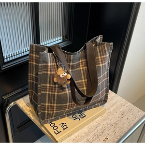 Close-up of vintage plaid tote bag with plush monster charm on books