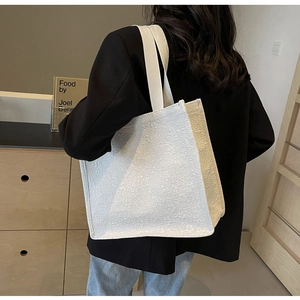 Minimalist white canvas tote bag shown as a spacious shoulder bag on a model in a home setting