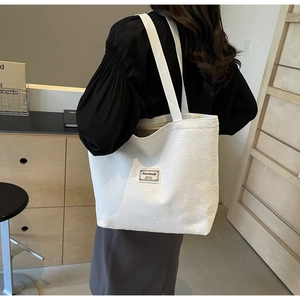 Detail view of the white tote bag showing the embossed heart patterns and woven strap