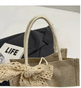 Detail of a beige linen tote featuring thick rope handles and a large lace bow accent